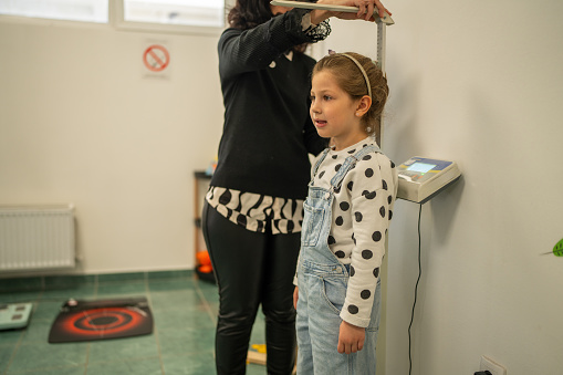 Mature female doctor measuring little girl's height at Healthcare Center. Periodical pediatric review concept