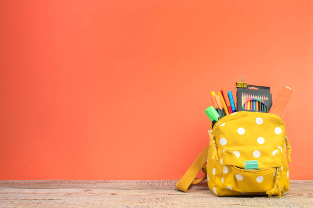 istock Yellow backpack with white polka dots with different colorful stationery on table. Orange background. Back to school. 2088659528