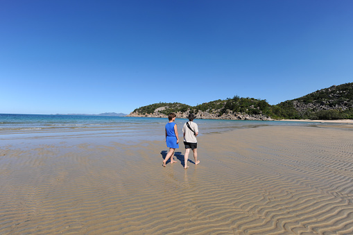 Woman and teenager seen from behind walking on idyllic tropical beach, Florence Bay, Magnetic Island, Queensland, Australia