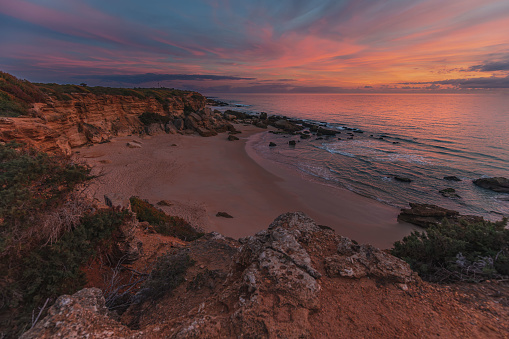The setting sun brings roseate hues to the sea and cliffs of one of the fossil-encrusted coves along the shoreline that is a protected environment hosting  rare types of Juniper, between Roche and Conil de la Frontera in Cádiz province in winter.