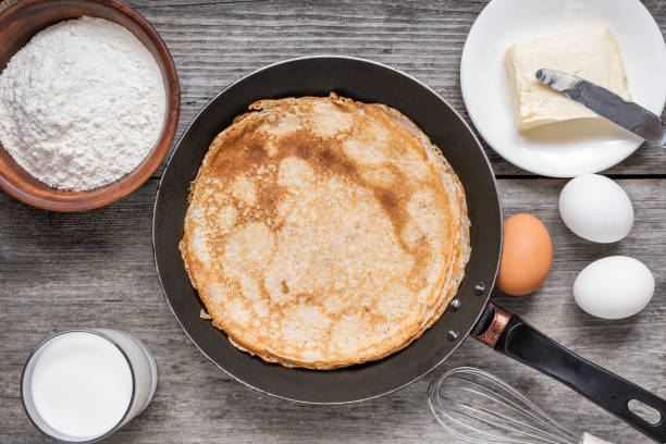 istock Frying pan with delicious crepes and ingredients for cooking on rustic wooden table. Thin pancakes in a pan with flour, eggs, milk and butter. Top view 2088703274