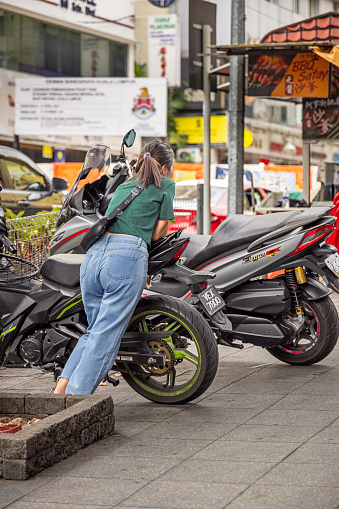 Kuala Lumpur, Malaysia - January 6th 2024:   Young woman having a break while leaning against a motorcycle