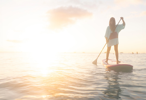 A female tourist enjoys stand-up paddle boarding, enjoys her vacation and the sea and peace and quiet