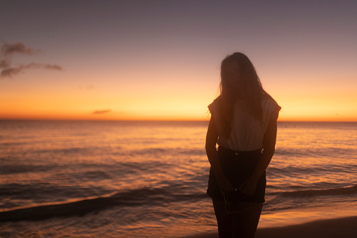 Silhouette of a woman standing in shallow sea water during sunset and looking directly into the camera