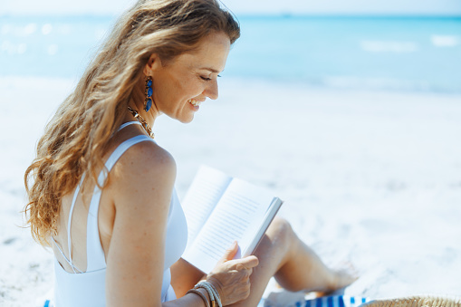 smiling modern female on the seashore with straw bag and book.