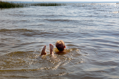 Boy learns to swim in river in summer. His legs stick out of water in funny way.