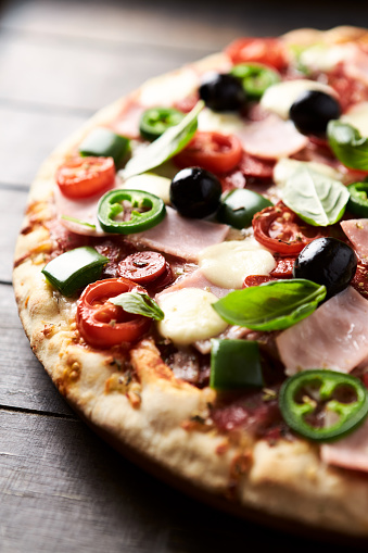 Pizza with ham, mozzarella cheese, cherry tomatoes, green and jalapeno pepper, black olives and fresh basil. Dark background. Close up.