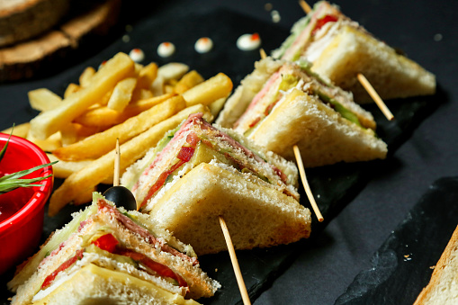 A black plate is filled with a selection of sandwiches and crisp golden French fries.