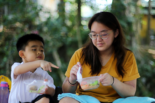 An Asian young boy is enjoying outdoor picnic with his family member
