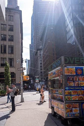 Manhattan, New York, USA - September 20, 2023: Food truck on a corner selling freshly prepared meals. Tourists walk by in the morning sun. A man photographing.