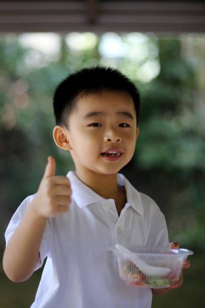 An Asian young boy is enjoying outdoor picnic eating joyfully