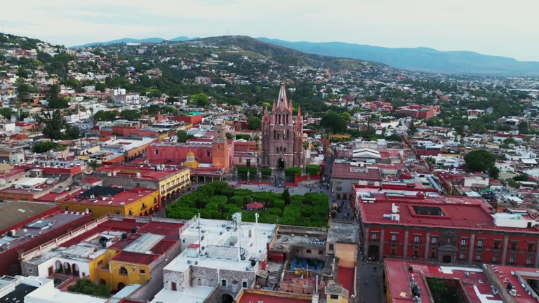 Panoramic sweep from the park and city center to the iconic Parroquia de San Miguel Arcangel in San Miguel de Allende, pan right, orbit