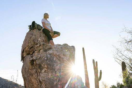 Mature woman pauses on rock above desert at sunset