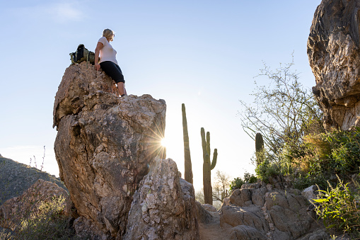 Mature woman pauses on rock above desert at sunset