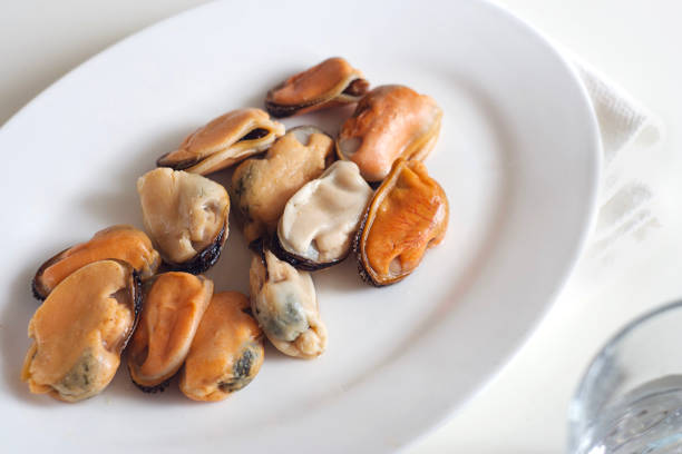 Mussels lie in a white plate on a white table