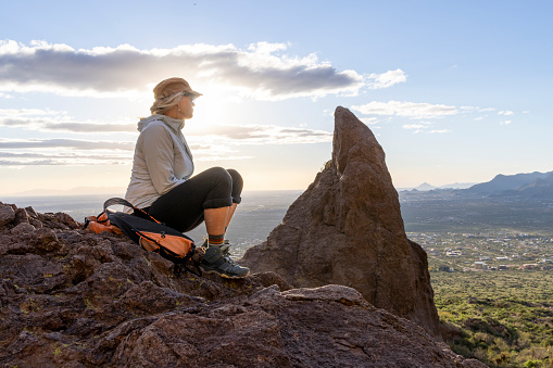Mature woman pauses on rock ridge crest above desert