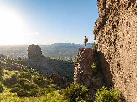 Hiker stands on rock pinnacle above desert and looks out