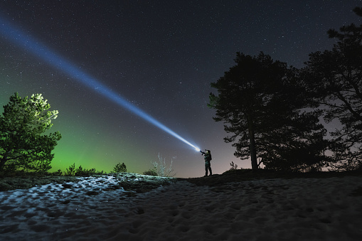 A soldier with a rifle and a flashlight in a night forest, sky with stars and northern lights. High quality photo