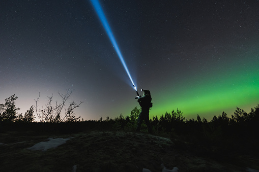 A soldier with a rifle and weapon flashlight in a night forest, sky with stars and northern lights. High quality photo