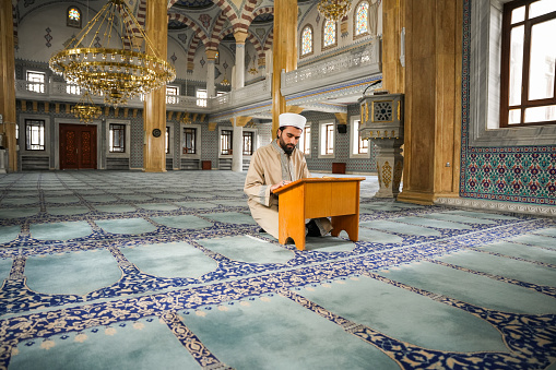 Young male imam reading the Quran in the mosque during Ramadan.
