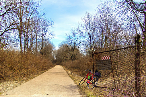 Early Spring landscape of a bike beside an open iron gate on the Great Sauk Trail passing through a forest on a sunny day near Prairie du Sac, Wisconsin.
