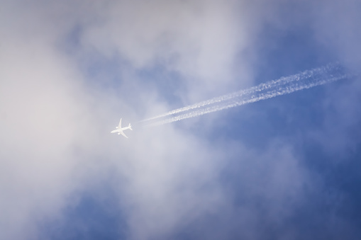 An airplane flies in a blue cloudy sky leaving a contrail, abstraction for background