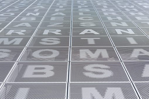 Exterior walls of a public parking lot covered with metal sheets with letters of the alphabet. This covering on the wall of a public parking lot provides shade and the passage of breezes into the parking lot.