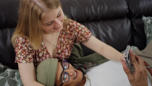 Loving young couple looking at phone photos while lying on a sofa