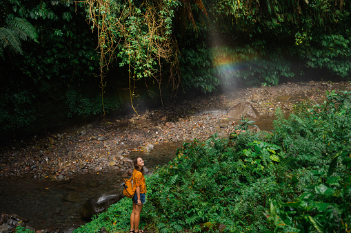 Woman standing near the refreshing river and rainbow in tropical jungles