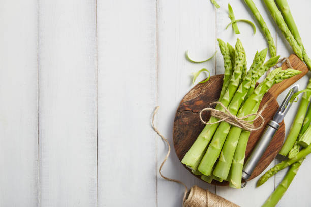 Peeling fresh green asparagus on wooden cutting board