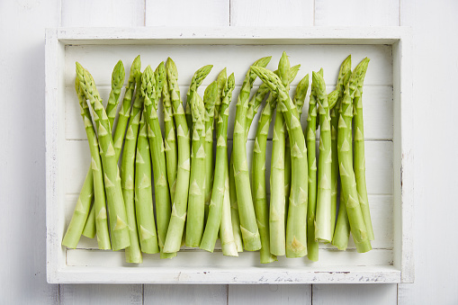 White wooden tray with fresh green asparagus, top view