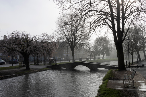 Bourton on the Water on a misty spring morning. This image captures the enchanting atmosphere as the village awakens. \n\nThe mist was hovering over the River Windrush and the charming stone bridges, adding a layer of tranquillity to this picturesque Cotswolds village, renowned for its scenic beauty and peaceful waterside setting.