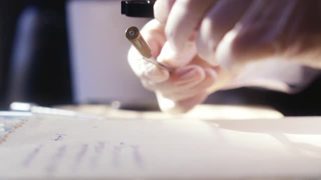 A forensics expert examines the bullet, working with a brush and magnifying glass