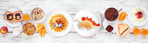 Fun child theme breakfast table scene with assorted animal themed foods. Top down view on a white wood banner background.