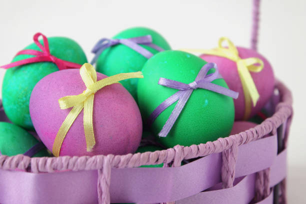 Multi-colored Easter eggs decorated with ribbons in a wicker basket on white background. Family religious traditions.