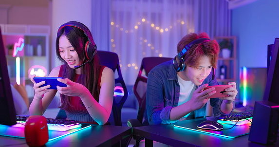 Asian young couple wear headset play online sports game on smartphone at home