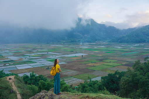 Serene woman with backpack standing on viewpoint looking at Sembalun Village on Lombok
