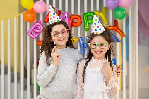 Two cute girls pose against a bright wall with balloons at a children's birthday party
