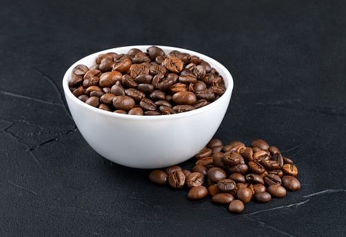 White ceramic bowl filled with roasted coffee beans on dark background