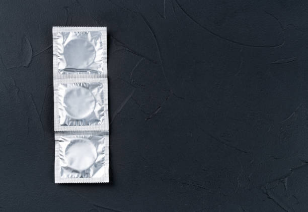 어두운 배경에 팩에 콘돔 3개 - contraceptive sex education birth control pill condom 뉴스 사진 이미지
