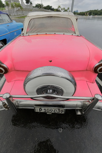 Havana, Cuba-October 07, 2019: American classic convertible cars -pink Ford Fairlane Sunliner 1956-blue Chevrolet Styleline DeLuxe 1950- parked under the rain on Revolution Square-Jose Marti Memorial.