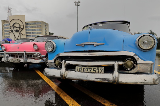 Havana, Cuba-October 7, 2019: American classic convertible cars (R - L), blue Chevrolet Styleline DeLuxe 1950-pink Ford Fairlane Sunliner 1956-blue Chevrolet Bel Air 1953, parked on Revolution Square.