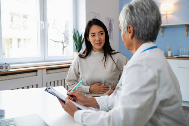 Female patient Japanese ethnicity describes stomach ache symptoms, to senior Caucasian female doctor During an annual medical check-up, female patient Japanese ethnicity explaining her stomach ache symptoms, to an senior Caucasian female doctor japanese female doctor stock pictures, royalty-free photos & images