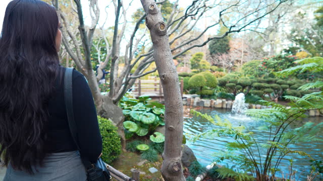 a slow-motion video depicting a beautiful young woman exploring a lush Japanese Tea Garden with fountains and a bridge in San Mateo, california