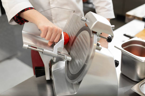 the chef in the restaurant kitchen prepares tomato slices with a slicer. - commercial kitchen restaurant retail stainless steel imagens e fotografias de stock