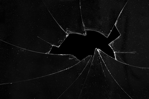 Cracks of broken glass, black background texture of a hole in a window