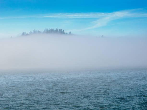 A breathtaking view of a mist-covered lake, snow-dusted village, and surrounding mountains in winter.