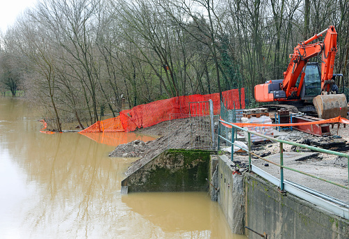 red excavator on the embankment of the river in flood during the flood in a road construction site