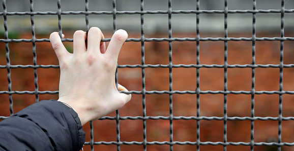 Iron bars of a reformatory and the hand of a young man clinging to the fence
