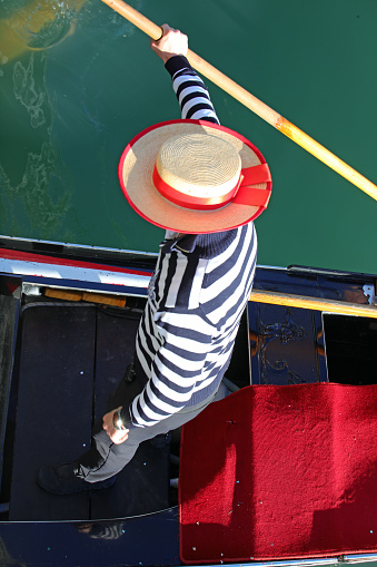 Gondolier with an hat rowing a gondola in a Venice canal photographed from above